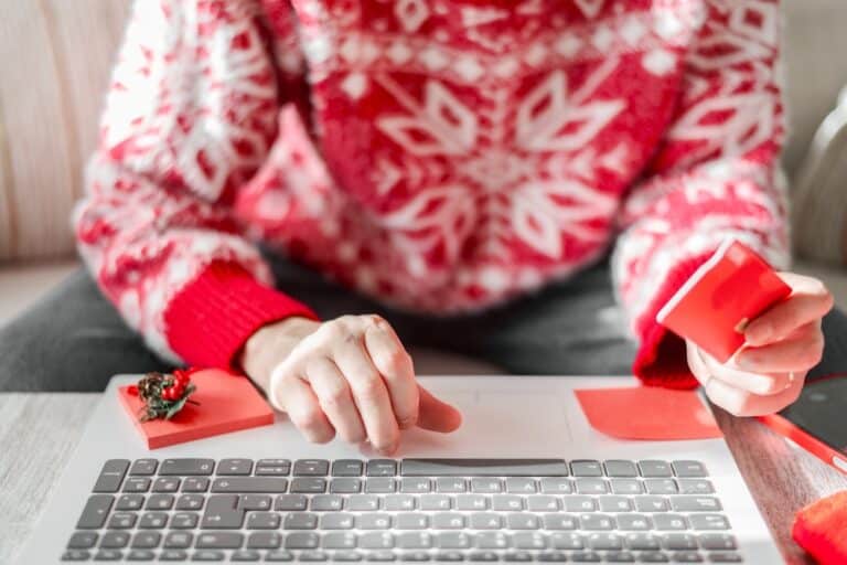 Business, Christmas, and Consumerism. Professional in Home Office Wearing Festive Attire, Securely Shopping Online with a Credit Card on a Laptop.