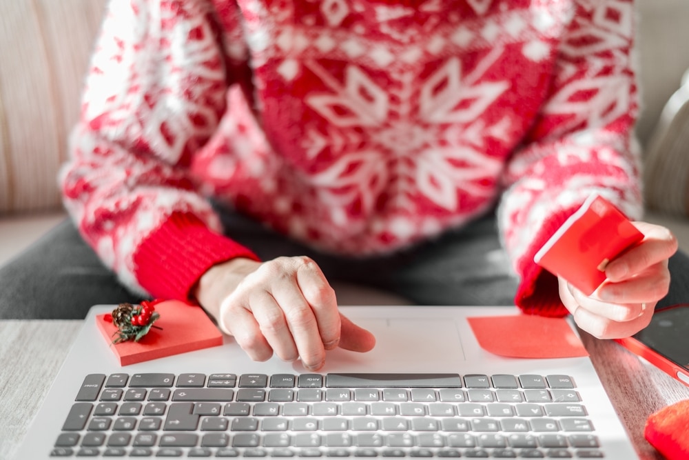 Business, Christmas, and Consumerism. Professional in Home Office Wearing Festive Attire, Securely Shopping Online with a Credit Card on a Laptop.